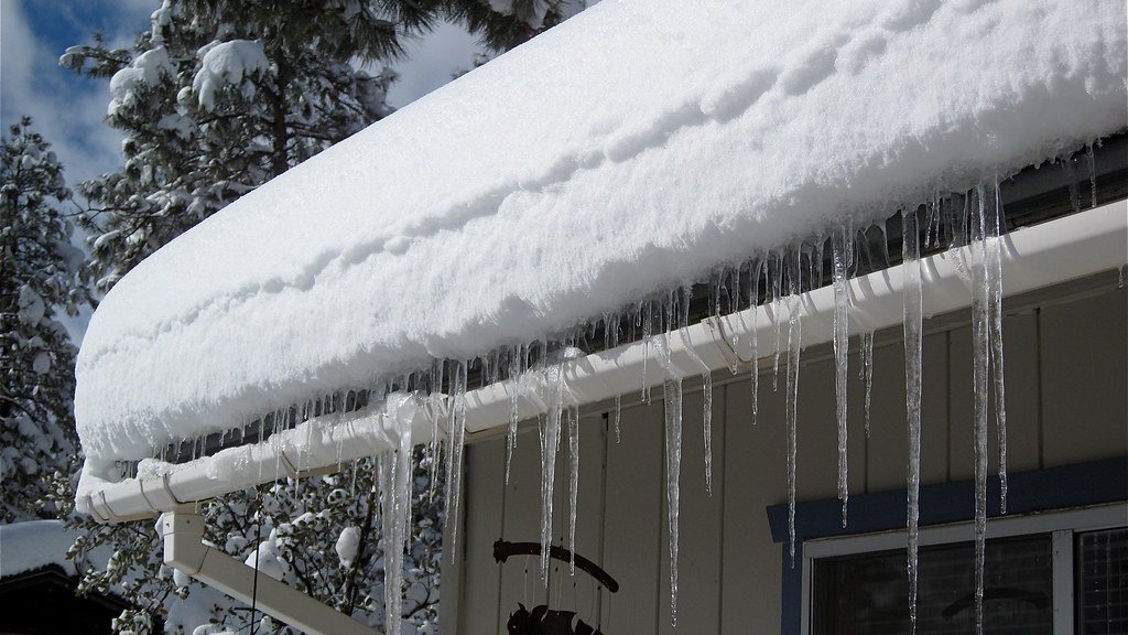 Glaçons pendant d'une gouttière sous un toit enneigé de maison